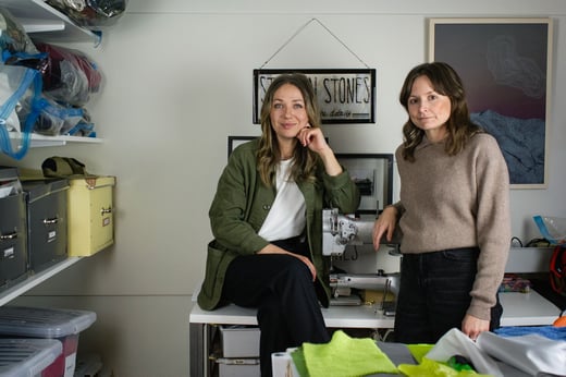 Emma och Anna från företaget Stitch N Stones i Åre. De står på sitt kontor, och vid sidan finns en hylla med textilspill de använder till sina accessoarer.