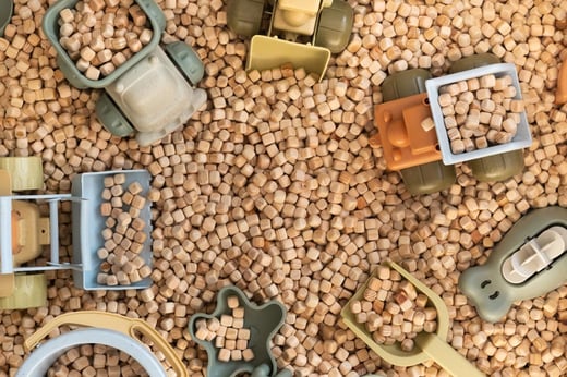 Leksaksfordon i naturfärger lastar träpellets, symboliserar cirkulära materialflöden och återvinning.